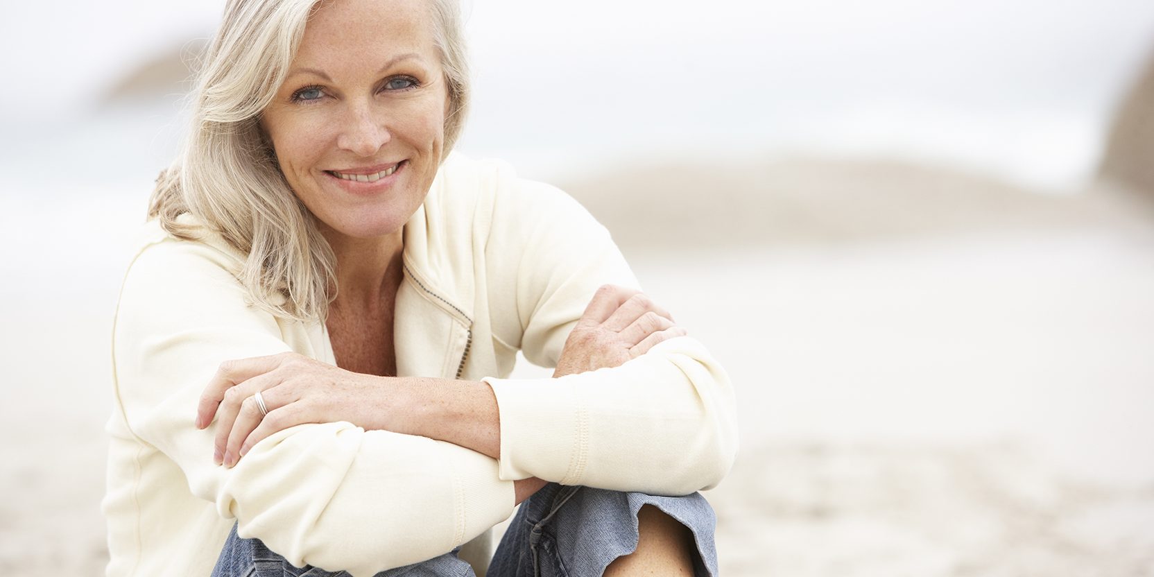 Senior Woman On Holiday Sitting On Winter Beach